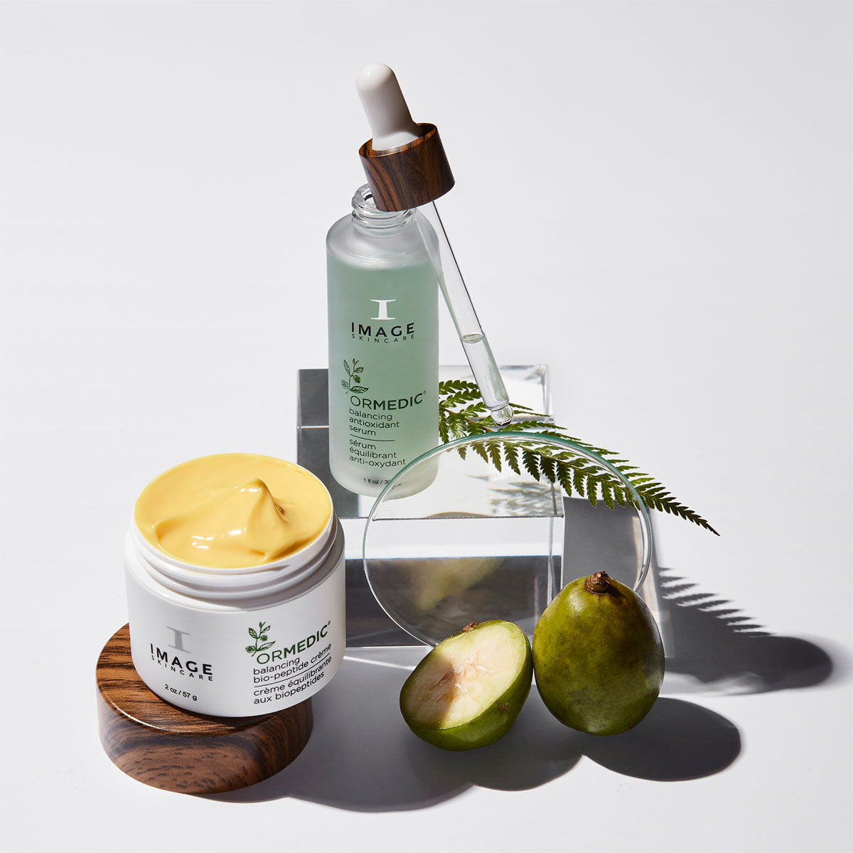 ormedic antioxidant serum and biopeptide creme on white background next to sliced fruit, plant leaf, and petri dish